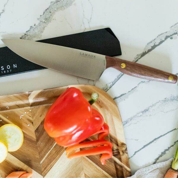 Vintage, walnut chef knife with red pepper on cutting board.
